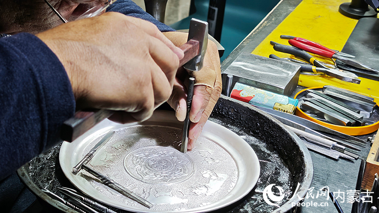 国家级非物质文化遗产代表性项目乌拉特铜银器制作技艺传承人巴图陶高对制作的银盘进行錾刻。人民网记者 张雪冬摄